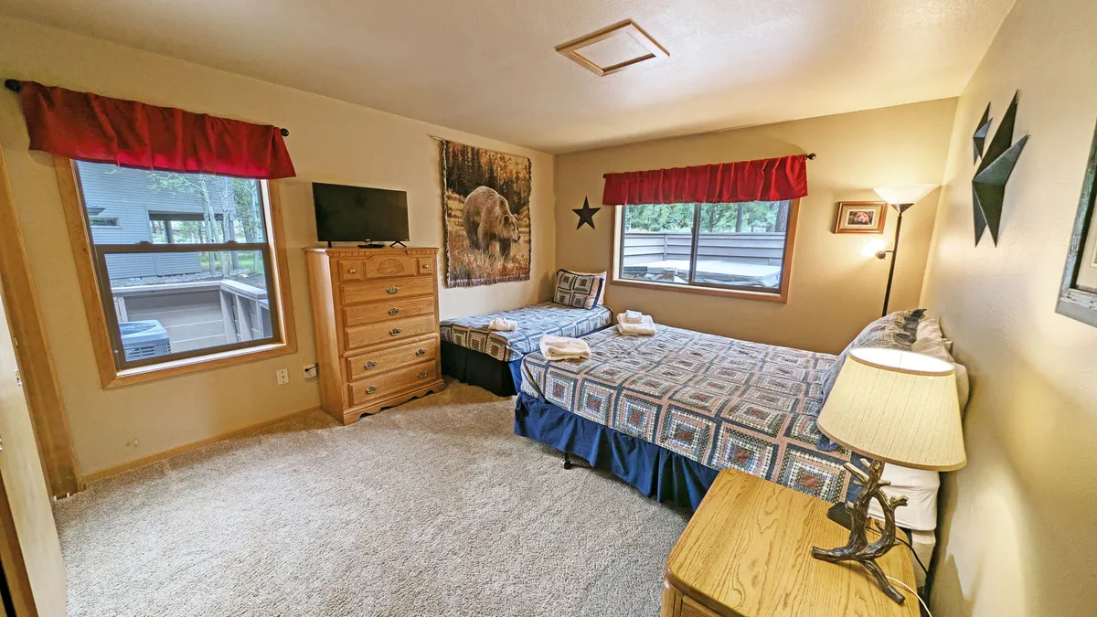 A welcoming bedroom with two beds, bear-themed wall art, a TV, dresser, and lamps. The space feels inviting and cozy, ideal for families or groups seeking restful, connected time together.