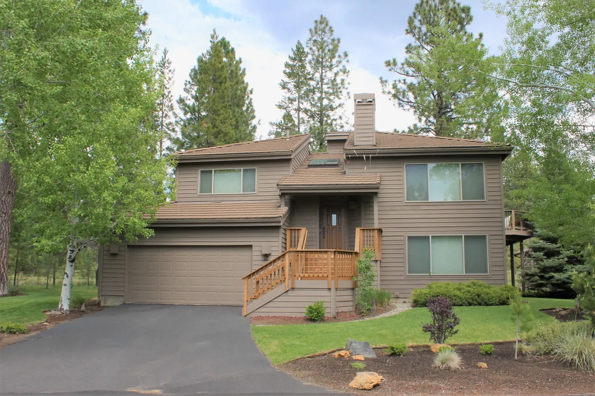 A welcoming front porch with wooden details, large windows, and a landscaped garden, evoking the feeling of arriving home to a peaceful retreat in the woods. The porch and garden area offer space for gatherings and relaxation, with direct visual access to the outdoors.