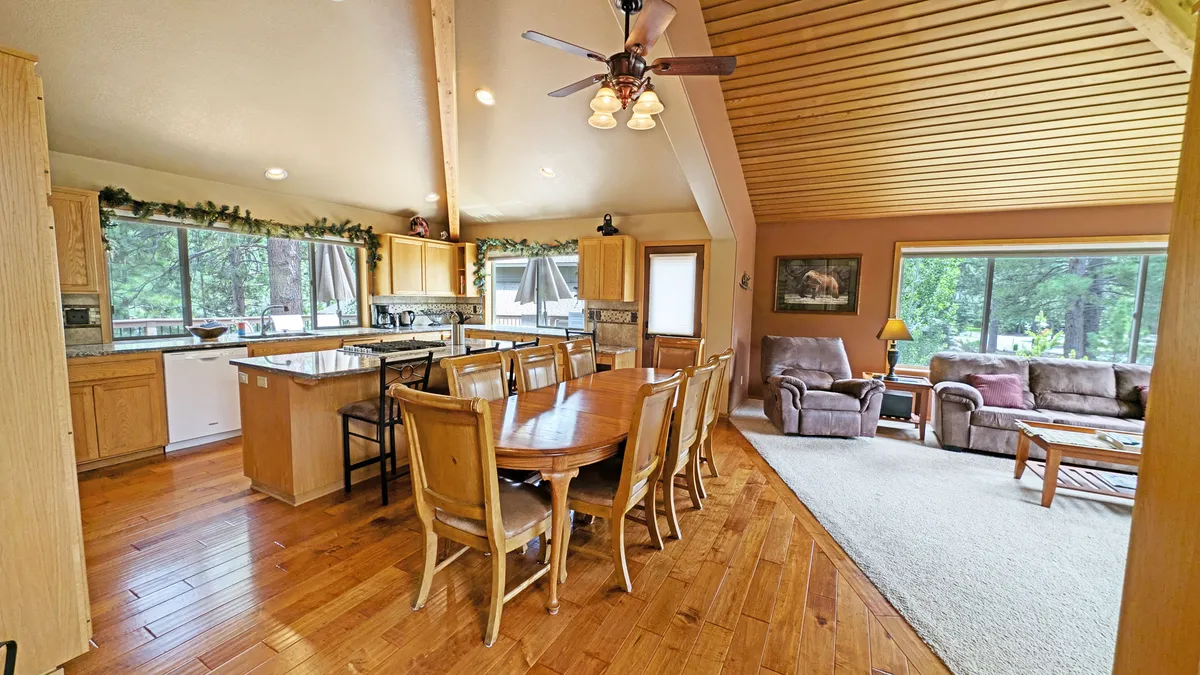 This image showcases a bright, open-concept living space with a dining table, kitchen island, comfortable seating, and large windows allowing natural light to fill the room. The layout conveys a sense of togetherness and warmth, perfectly suited for family meals, social gatherings, and relaxing moments.