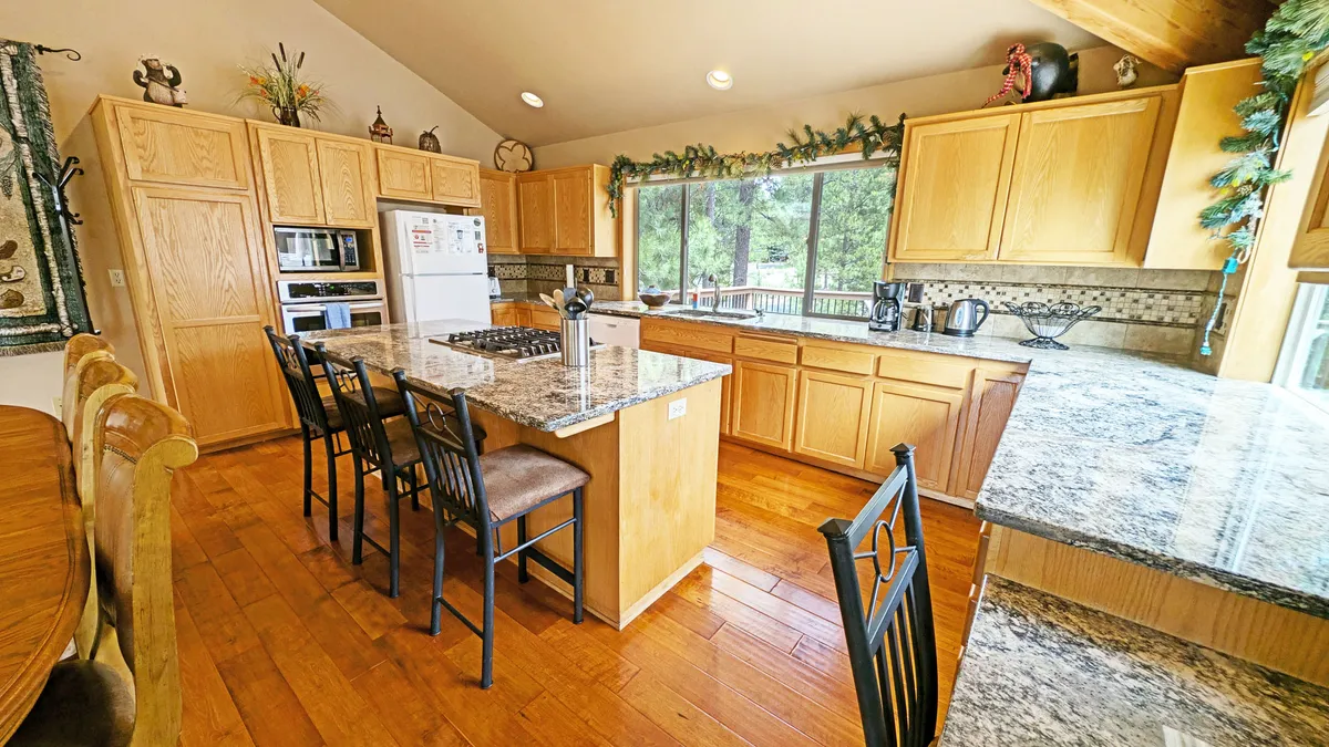 This photo focuses on the kitchen, highlighting the granite countertop, kitchen island with bar seating, and a large window that adds to the sense of airiness. Warm wooden cabinetry and inviting seating suggest a perfect space for cooking and casual gatherings.